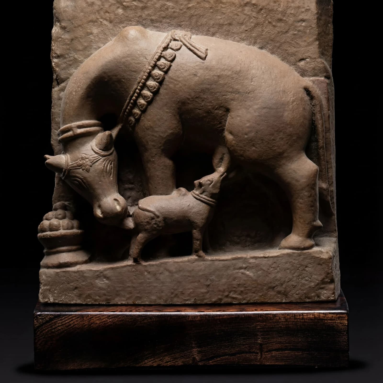 A side-profile view of the Kamdhenu Sculpture, a stone composite replica showing a cow nursing its calf.