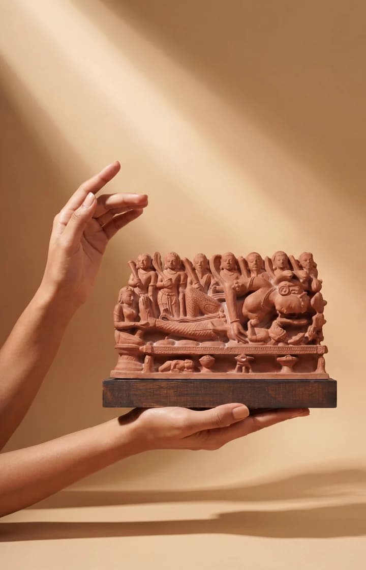Hands gently cradle the Krishna's Birth Sculpture, a terracotta-style museum replica featuring intricate figures of Devaki and soldiers.