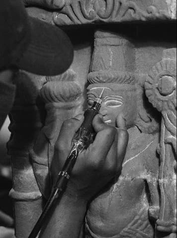 An artisan uses a precision rotary tool to carve intricate details into a sandstone museum-replica sculpture.