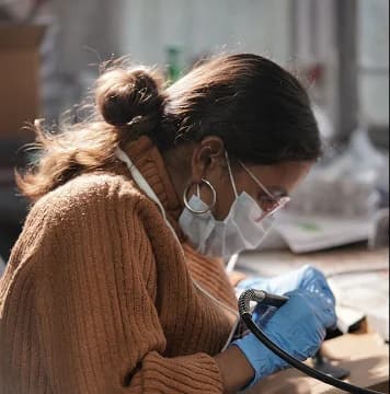 An artisan wearing a protective mask and blue gloves carefully hand-finishes a museum-replica artifact in a sunlit studio.