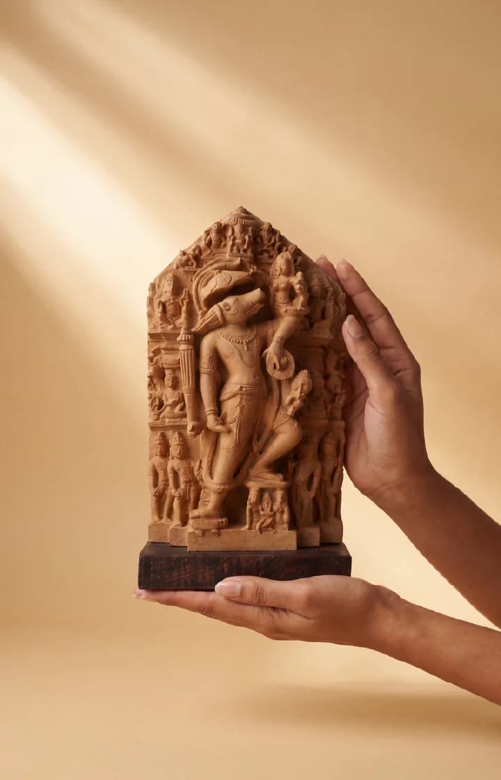 A pair of hands holds a detailed stone composite Nar Varaha Sculpture, showcasing the intricate man-boar deity relief.