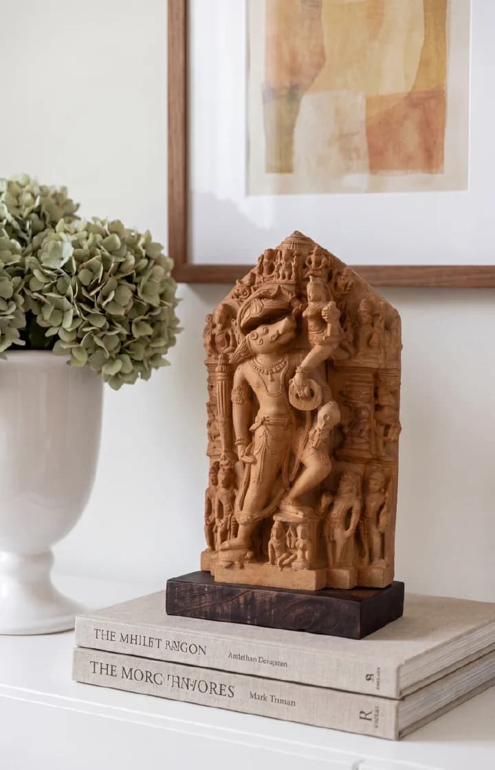 A Nar Varaha Sculpture replica in stone composite displayed on a stack of books next to a vase.