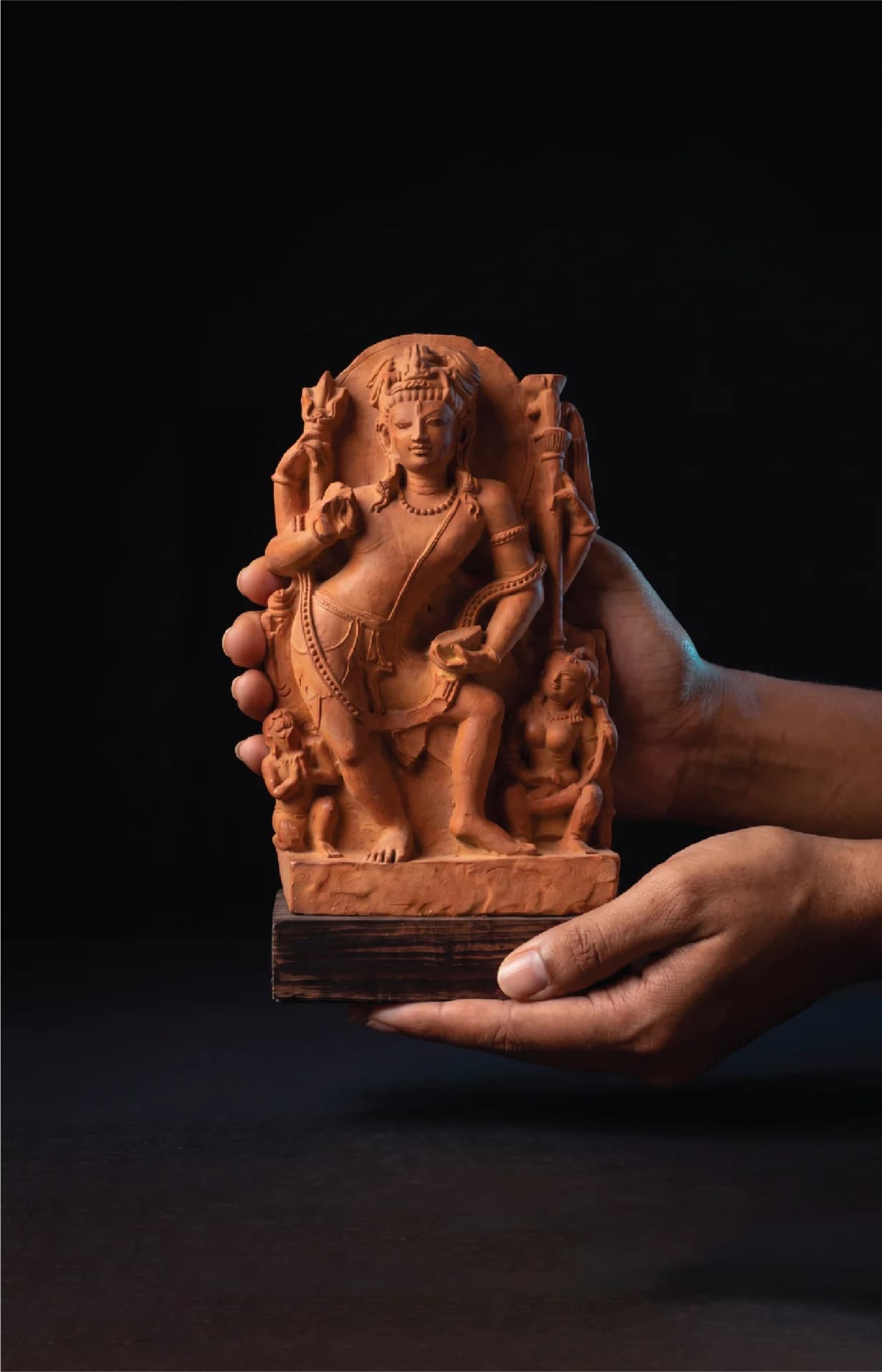 A pair of hands holds a hand-finished stone composite Natesh Shiva Sculpture against a dark, minimalist background.