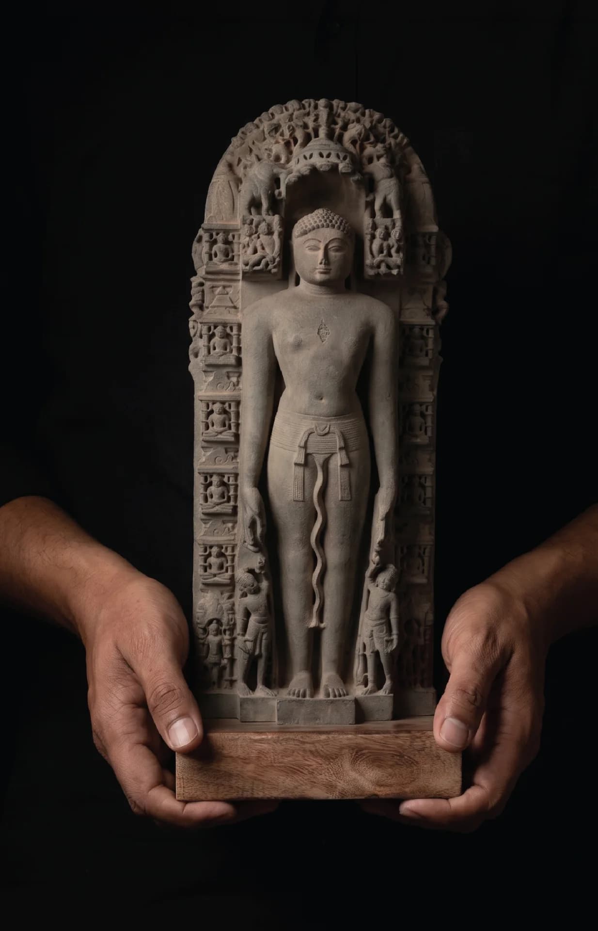A pair of hands holds a stone composite Parshvanath Sculpture, showcasing the intricate 11th-century style museum replica details.