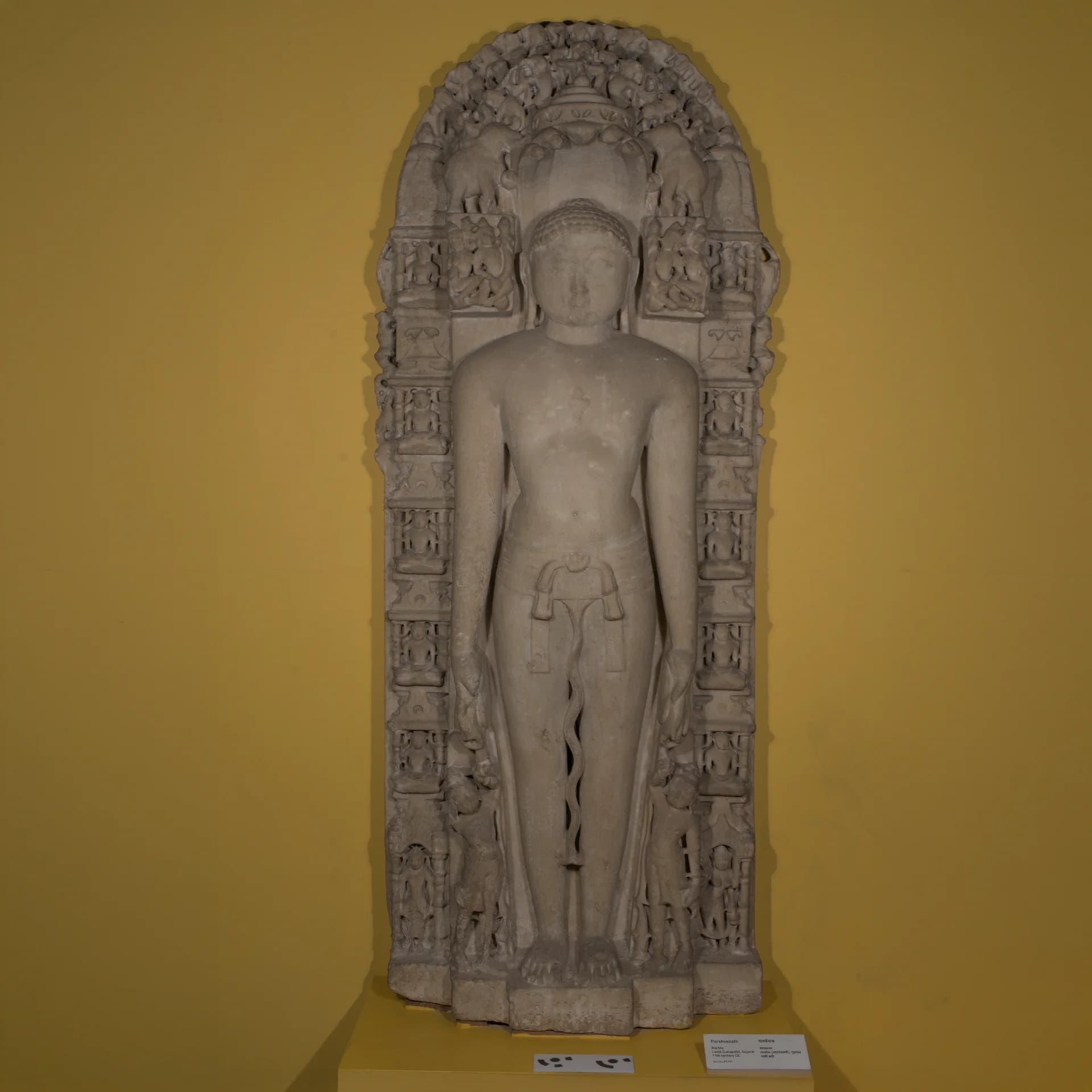 A full-length front view of the Parshvanath Sculpture, a stone composite replica featuring intricate carvings and a serpent canopy.