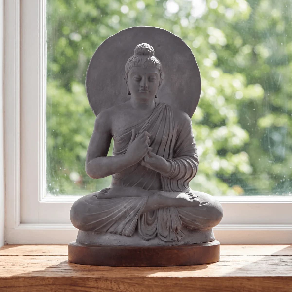 A front-facing view of the Preaching Buddha stone composite statue, seated in meditation against a bright window background.
