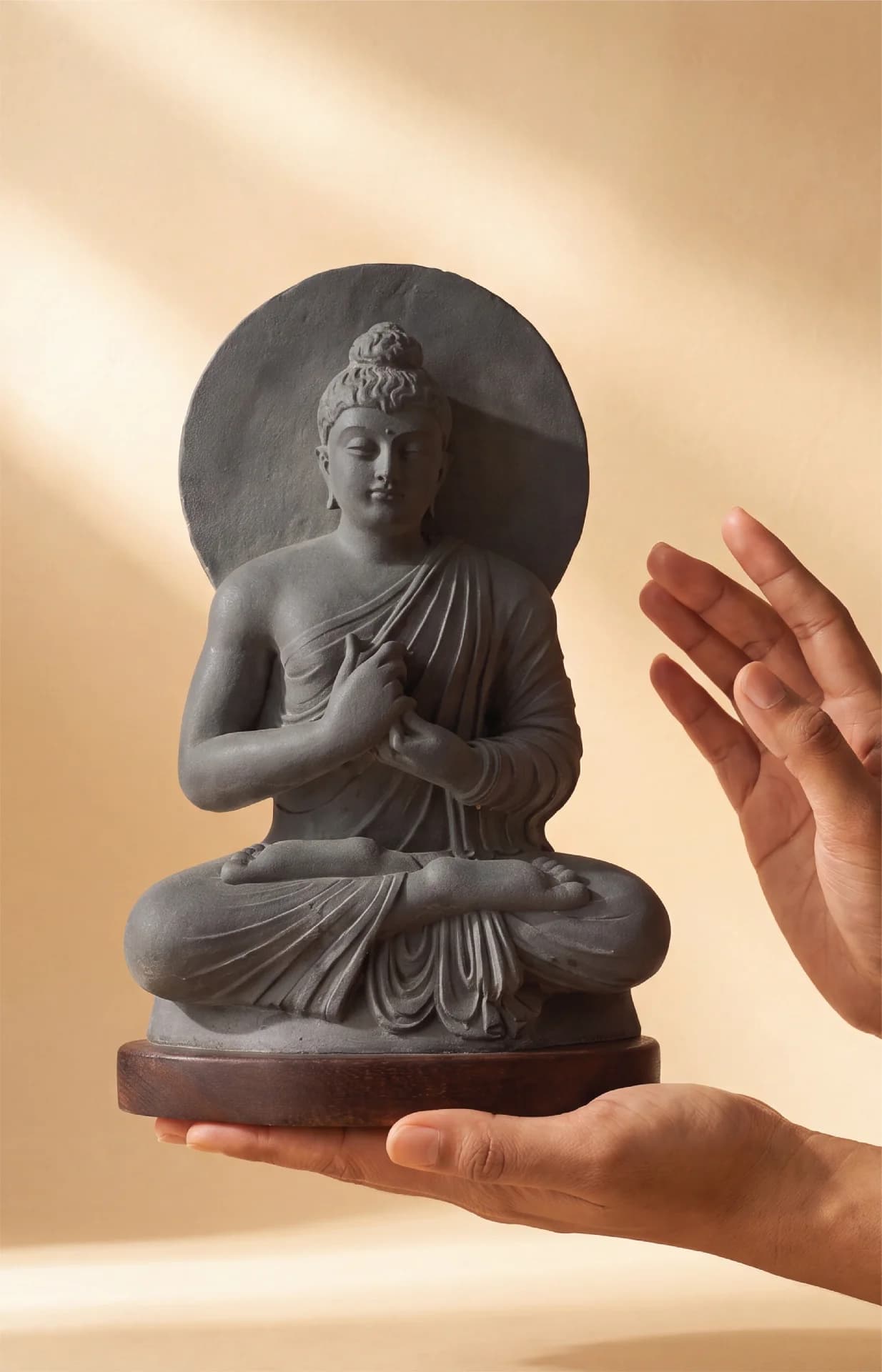 A pair of hands gently cradles a stone composite Preaching Buddha statue, showcasing its intricate Gandhara-style robe details.