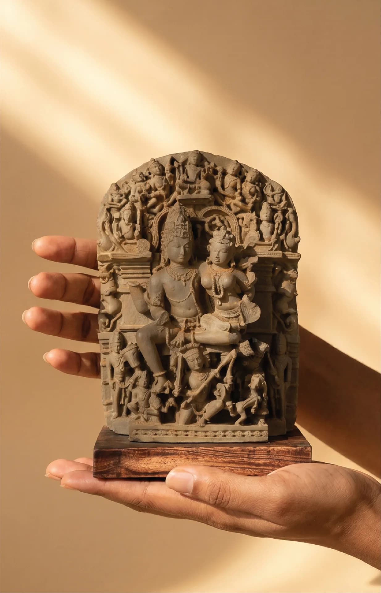 A pair of hands holds a hand-finished stone composite Ravananugraha Sculpture, showcasing intricate 11th-century temple art details.