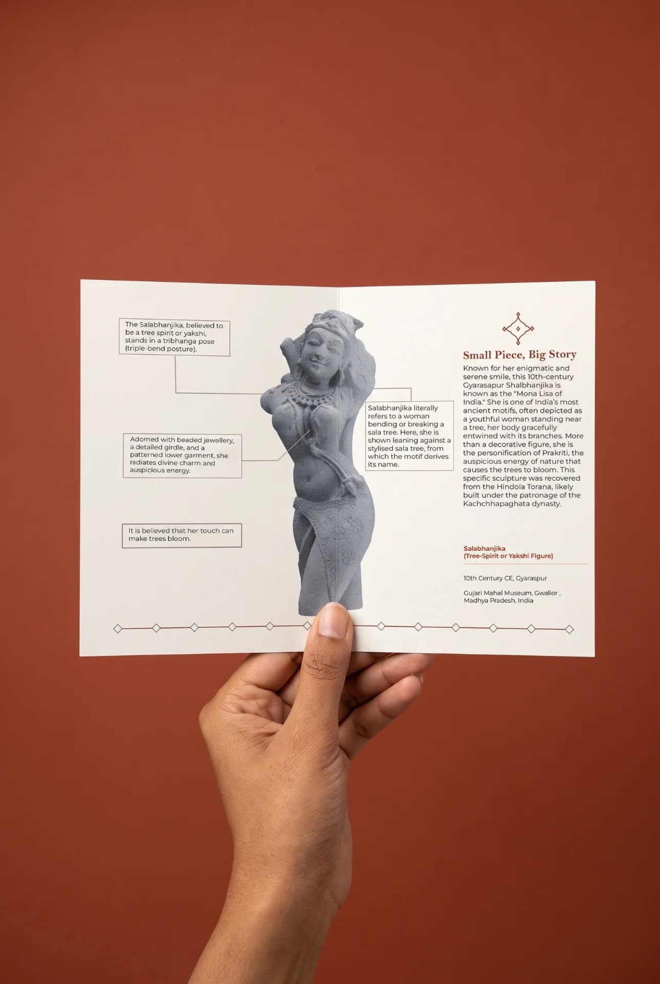 A hand holds an informational brochure about the Salabhanjika Sculpture, featuring a detailed stone composite illustration and historical context.