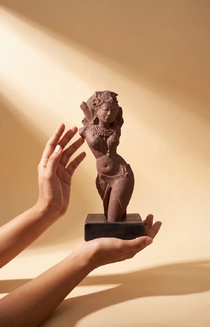 A pair of hands gently cradles the Salabhanjika Sculpture, a hand-finished stone composite replica featuring an elegant tribhanga pose.