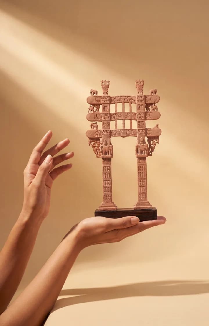 A pair of hands gently cradles a Sanchi Torana Gateway Miniature, showcasing the intricate sandstone-style carvings against a soft background.