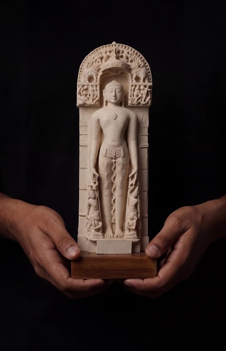 Two hands hold a Shantinath Sculpture museum replica, featuring intricate marble-style carving of a Tirthankara in an arched niche.