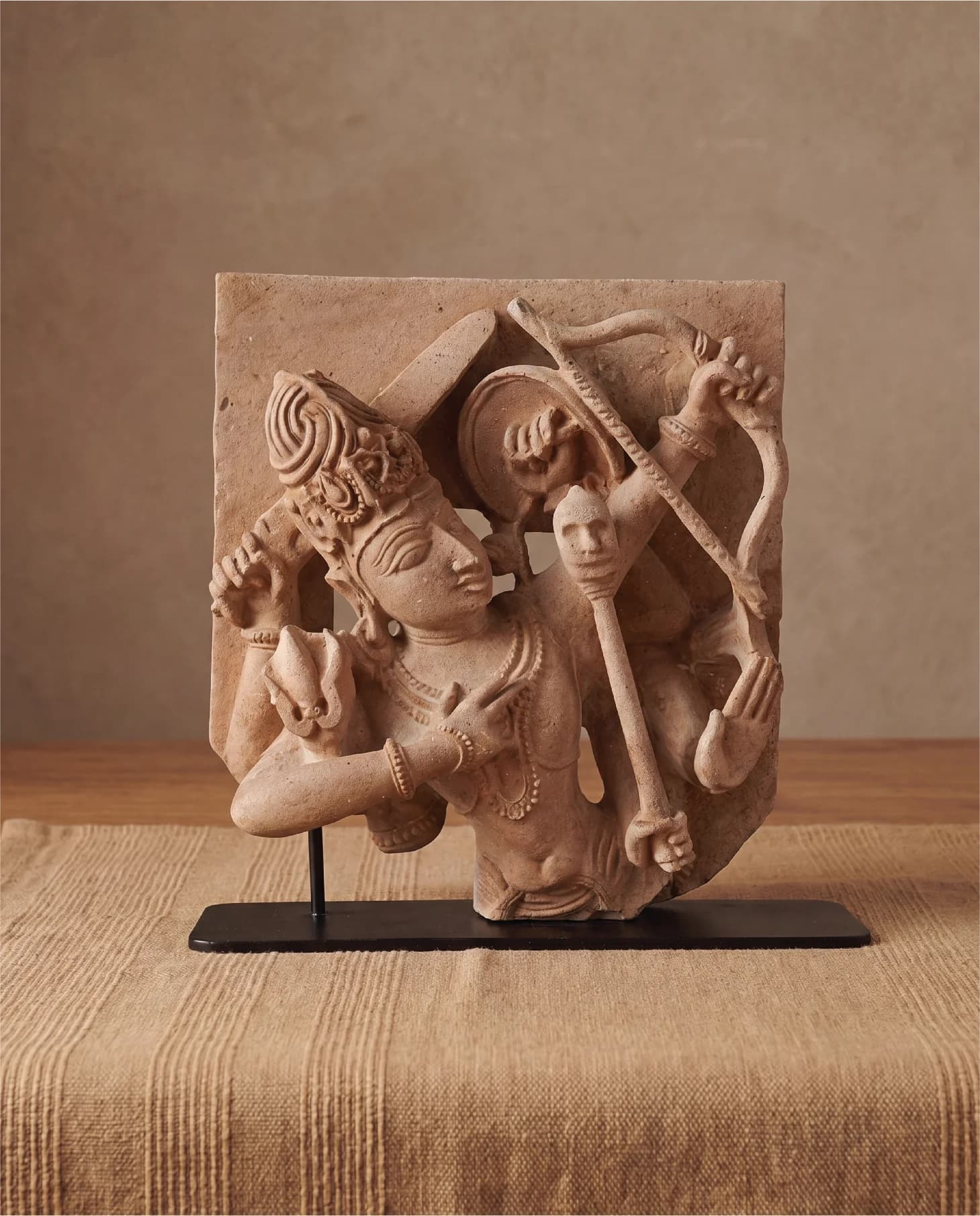 A stone composite Tripurantaka Shiva sculpture on a black metal stand, showing the deity holding a bow and arrow.