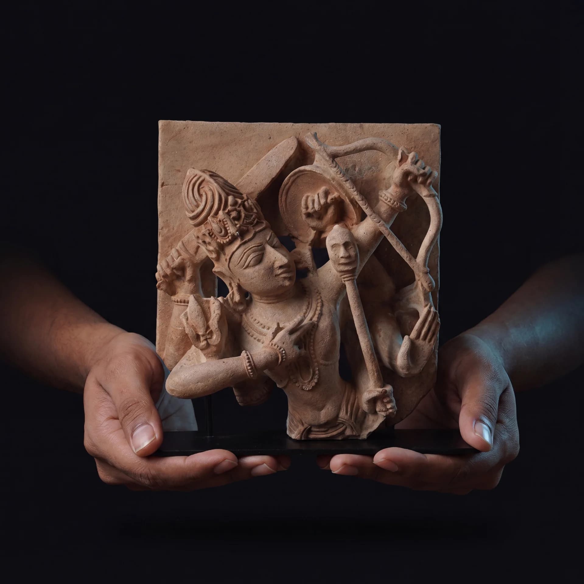 A pair of hands holds a stone composite Tripurantaka Shiva sculpture, showcasing the intricate relief details of the cosmic archer.