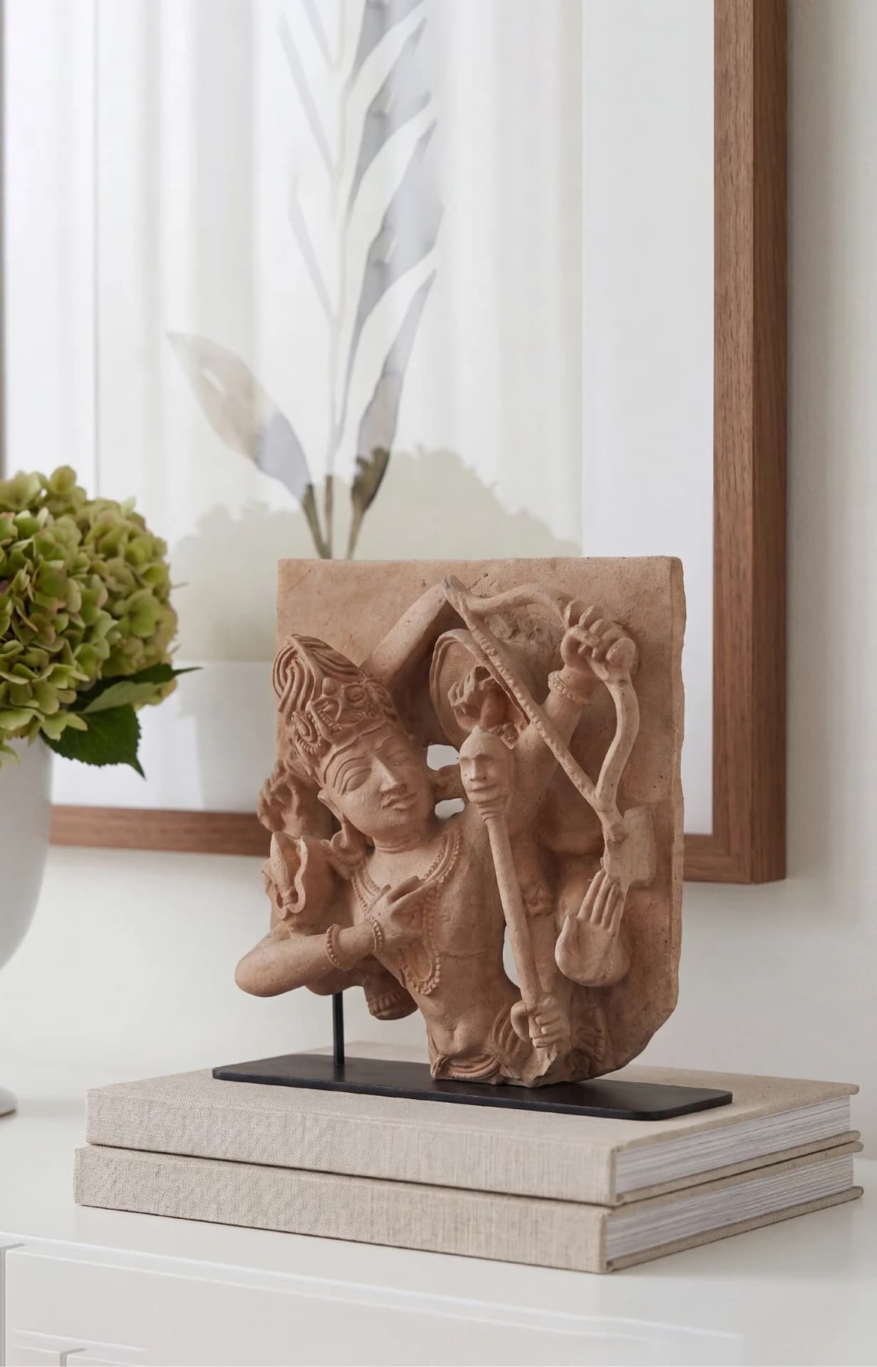 A stone composite replica of Tripurantaka Shiva displayed on a stack of books, showcasing intricate relief carving details.