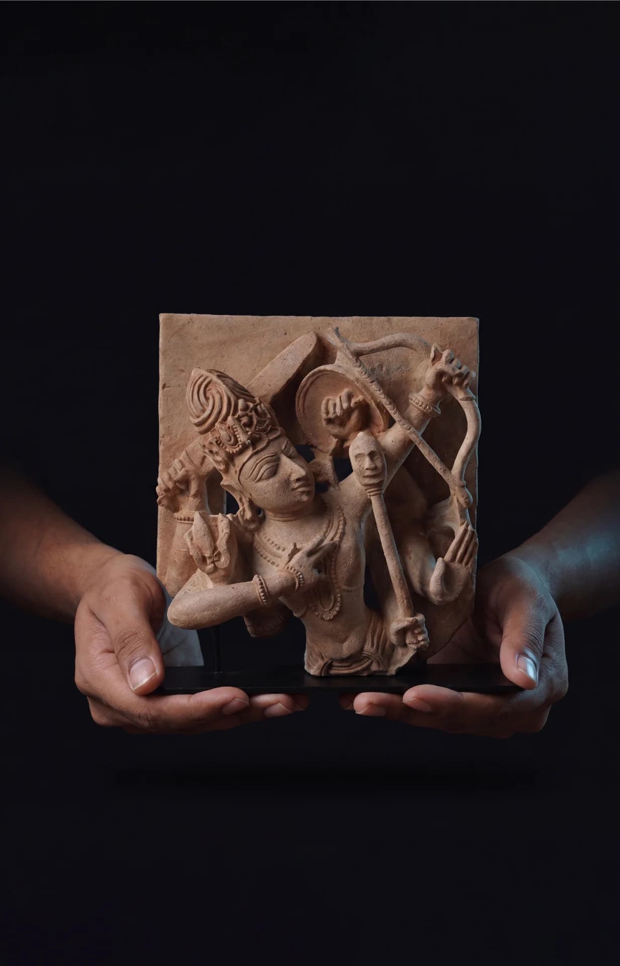Two hands hold a stone composite Tripurantaka Shiva sculpture, highlighting the intricate relief details of the cosmic archer.