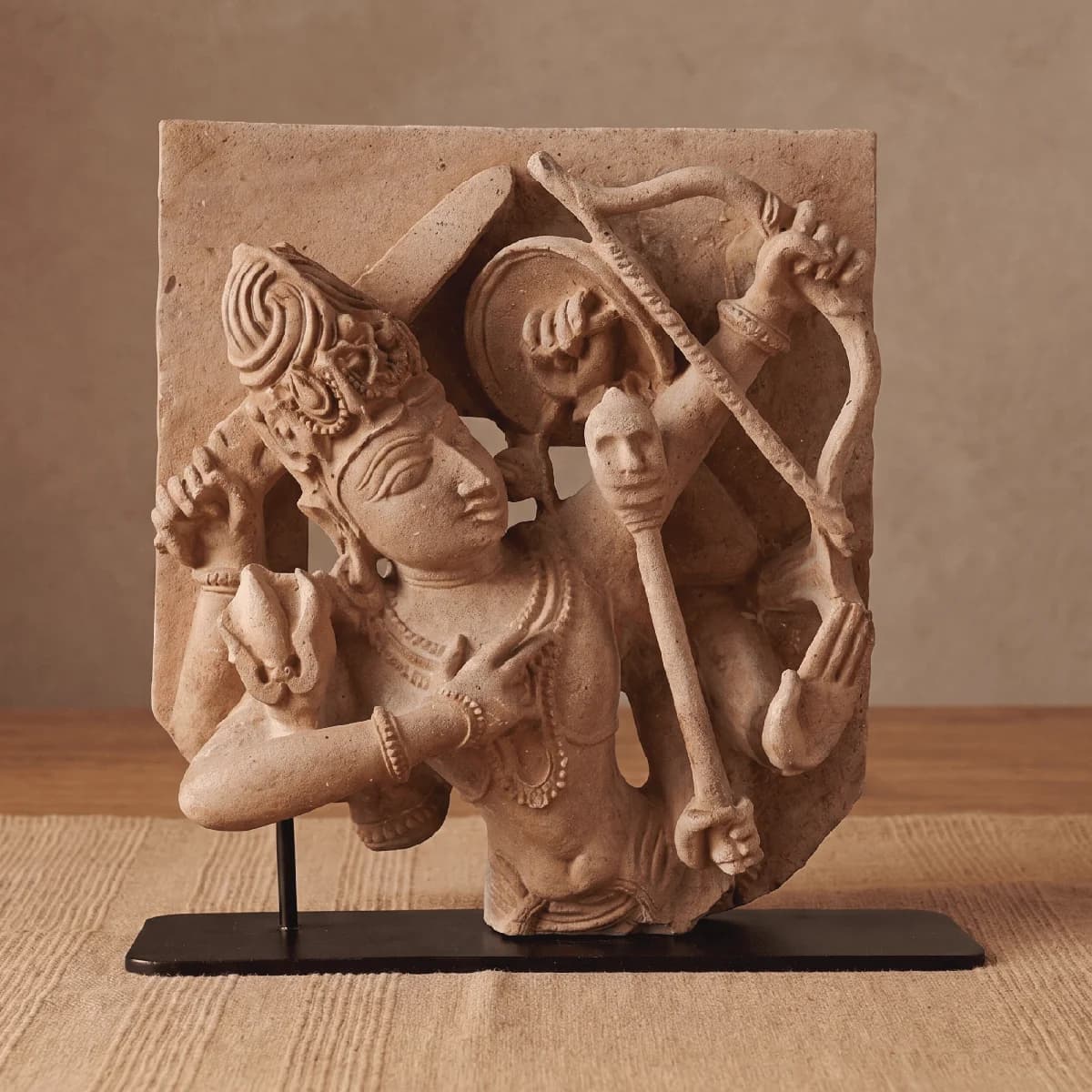 A stone composite Tripurantaka Shiva Sculpture replica showing the deity holding a bow, displayed on a black metal stand.