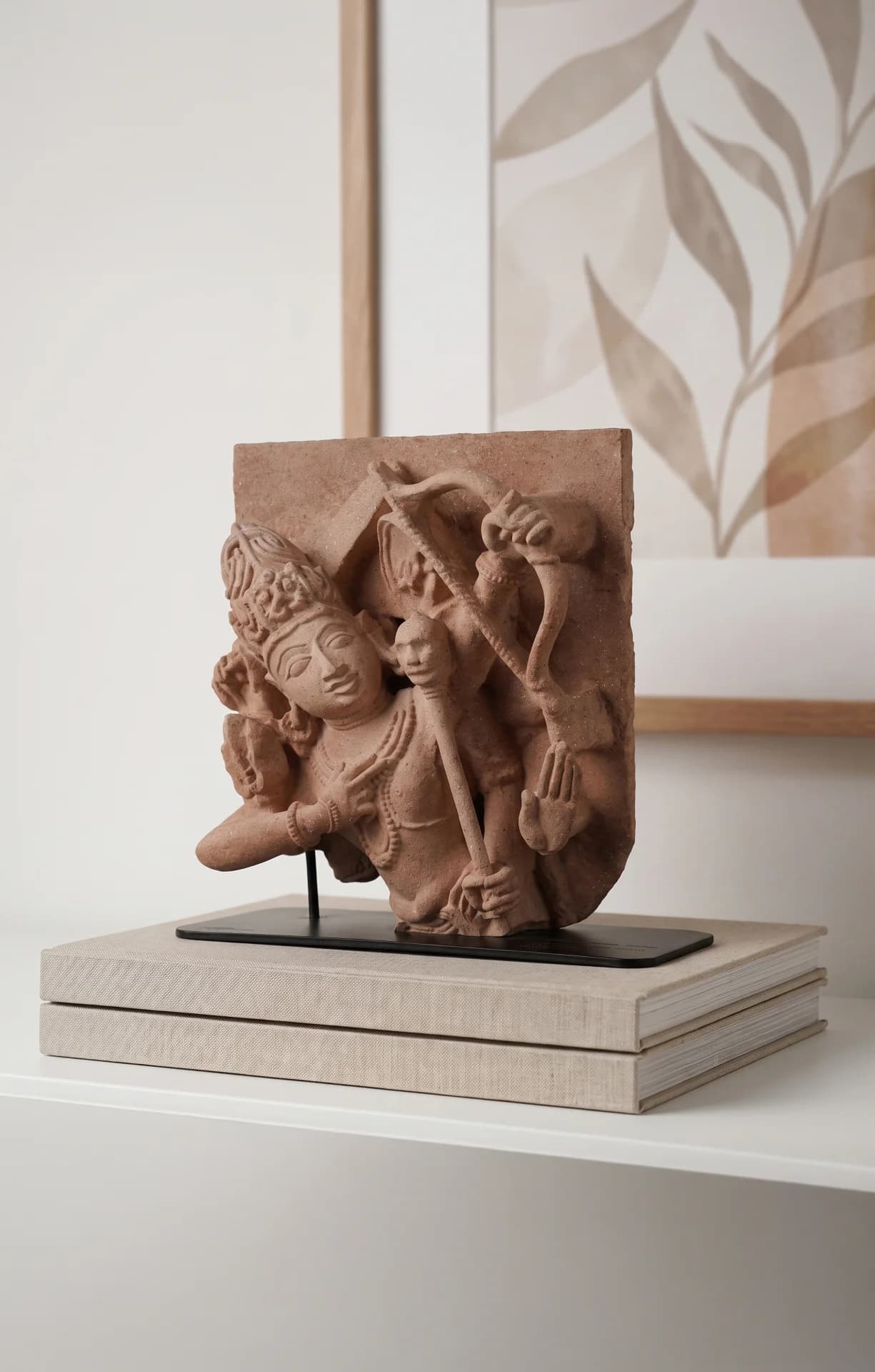 A stone composite Tripurantaka Shiva Sculpture replica displayed on a modern black stand atop stacked neutral books.