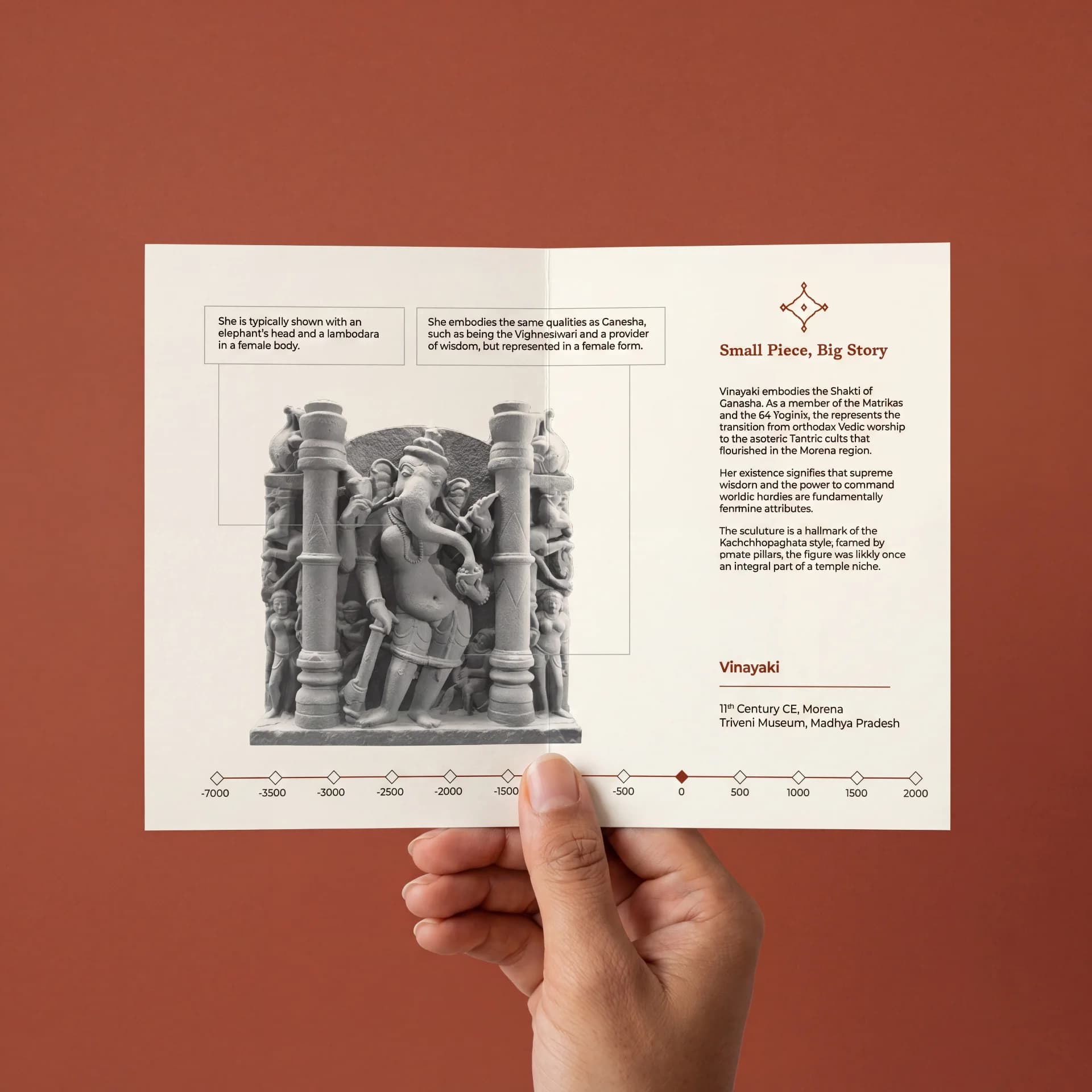A hand holds an informational brochure featuring the Vinayaki Sculpture, a detailed stone-style replica with historical context and descriptive annotations.