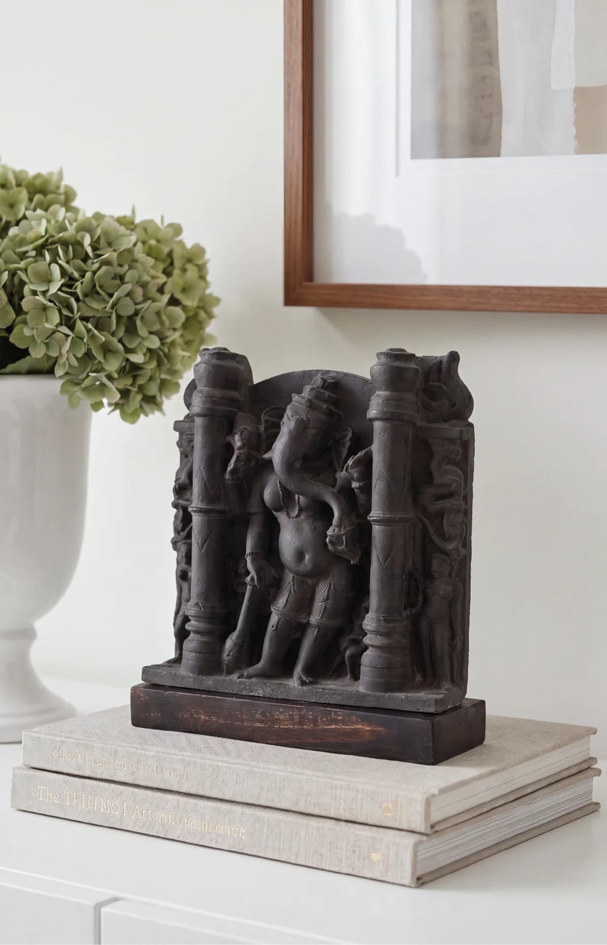 The Vinayaki Sculpture museum replica displayed on a stack of books, showcasing intricate stone-finish temple iconography in a home setting.